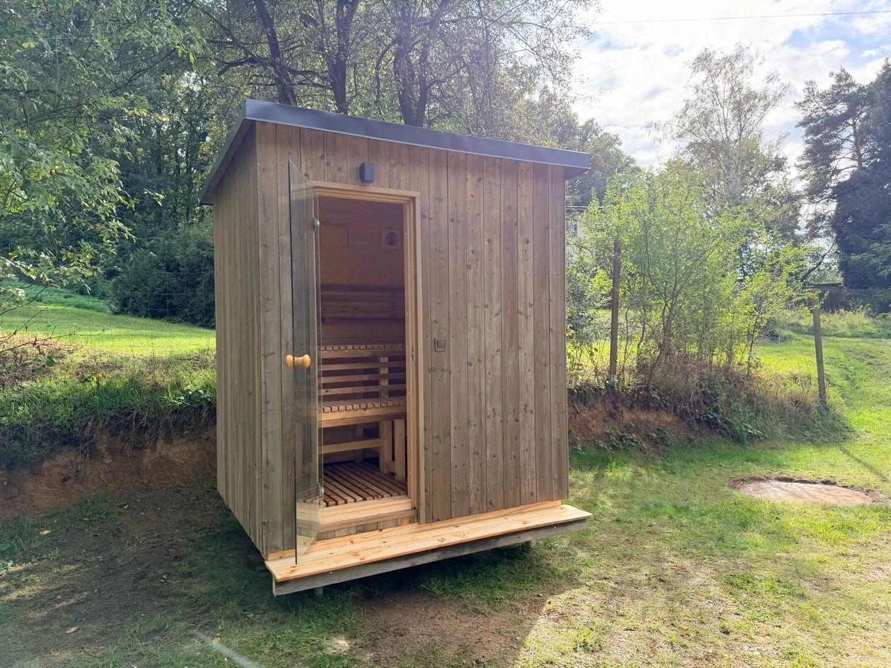 Gartensauna in Holzrahmenbauweise mit Pultdach und Glastür auf einer Wiese