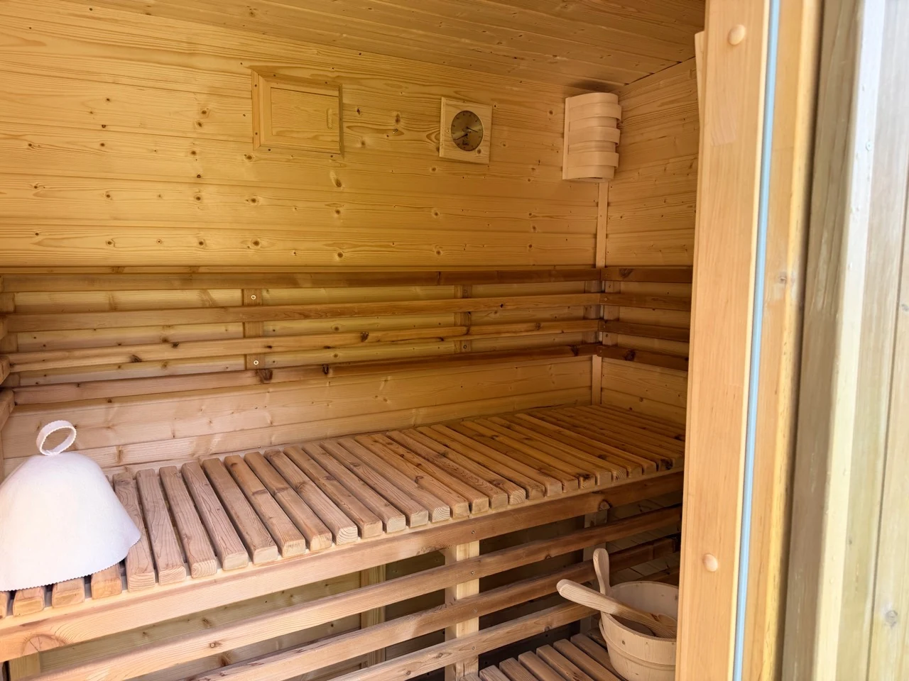 Innenraum einer selbst gebauten Sauna mit Lattenbänken, Thermometer und Saunakübel